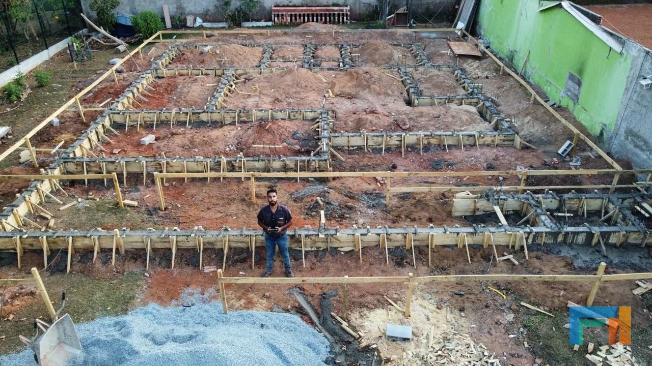 Engenheiro em pé sobre fôrmas de fundação, com controle de drone
